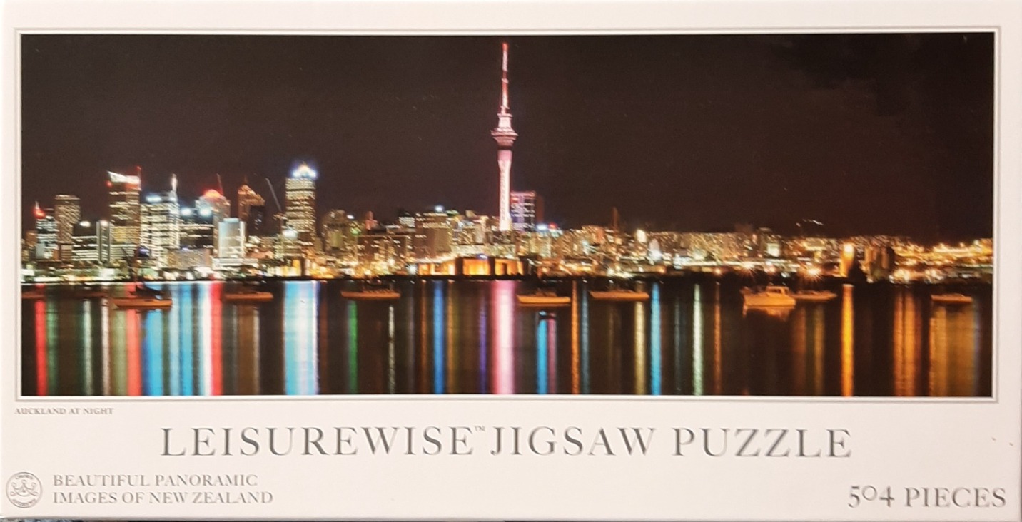 A panoramic night view of the Auckland city skyline featuring the illuminated Sky Tower and its harbor reflections.