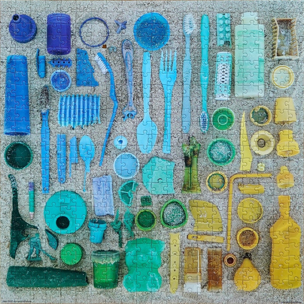 An assortment of blue, green, and yellow plastic debris arranged in a grid-like pattern on a sandy background.