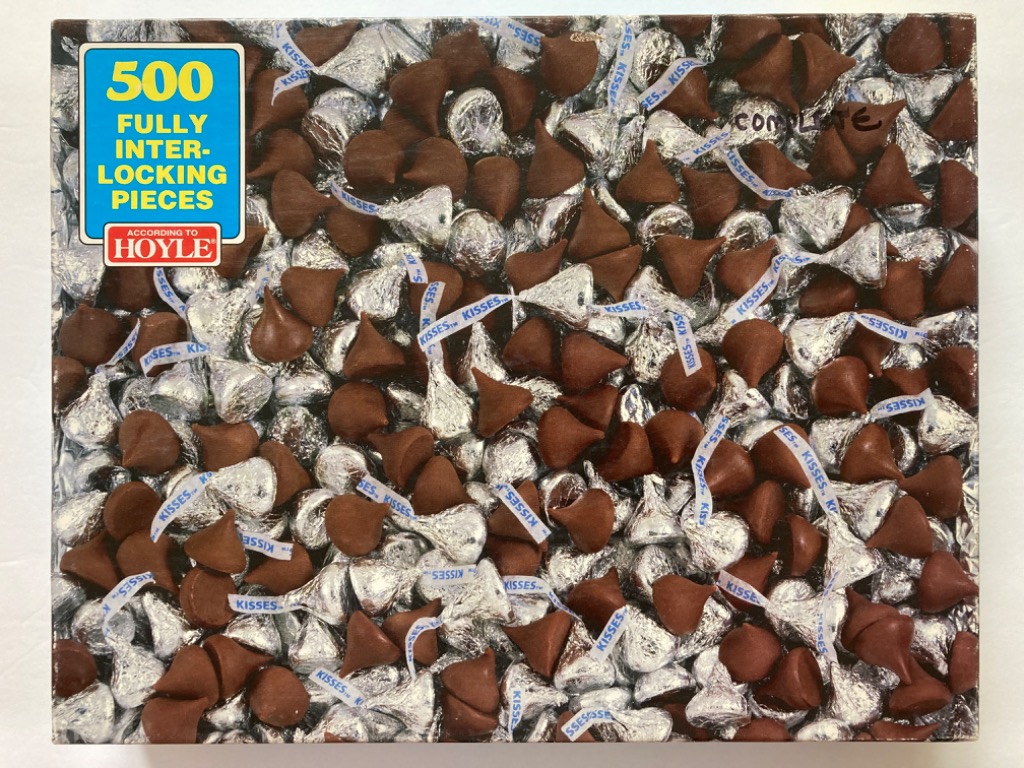 A top-down photographic view of many chocolate candies wrapped in silver foil with white paper plumes.