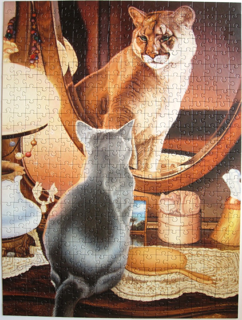 A grey house cat sitting on a vanity and looking into a mirror where it sees a mountain lion reflection.