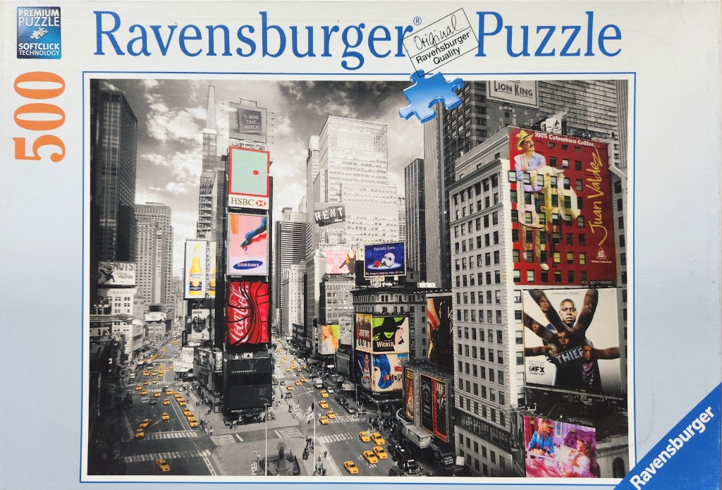 A black and white photograph of Times Square in New York City with colorful billboard advertisements throughout.