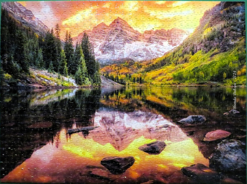A photograph of the Maroon Bells reflected in a calm, vibrant lake at sunset with autumn foliage.