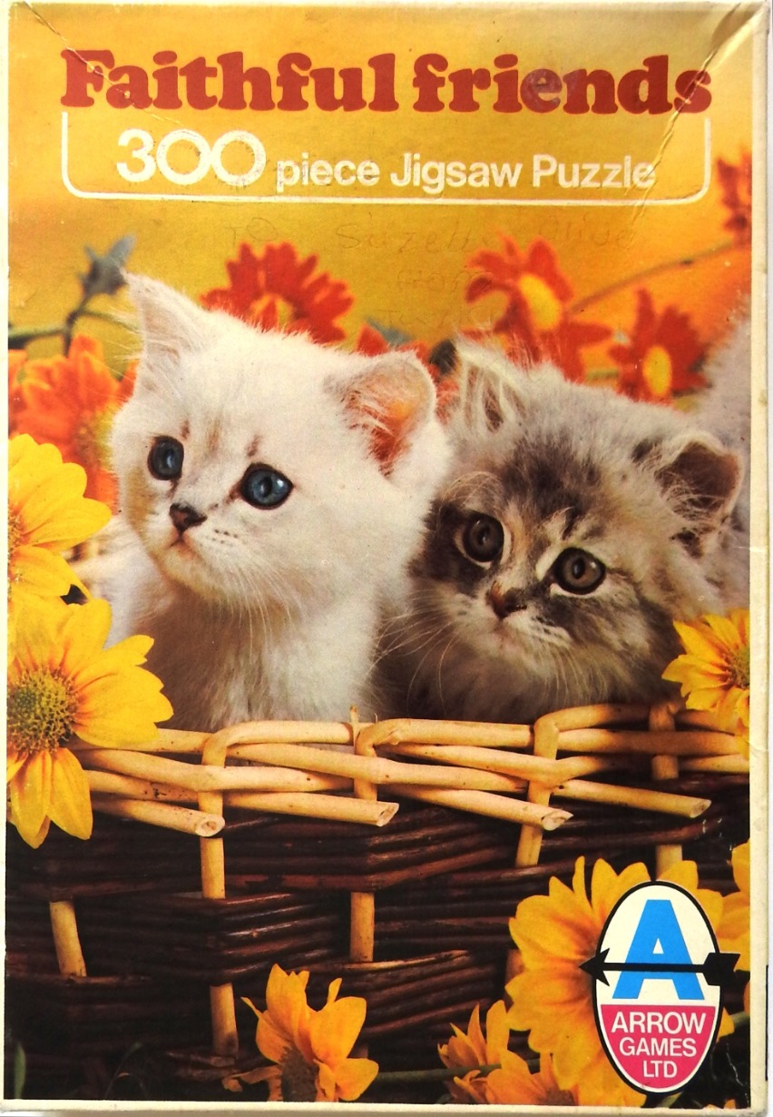 Two fluffy kittens, one white and one grey, sitting in a woven wicker basket surrounded by bright yellow and red flowers.