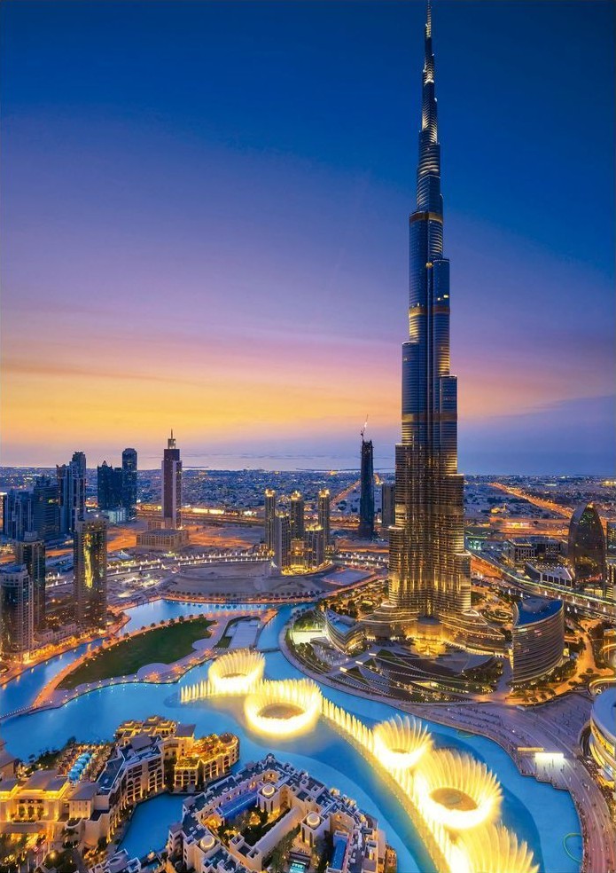 Aerial view of the Burj Khalifa tower and the surrounding Dubai Fountain at sunset.