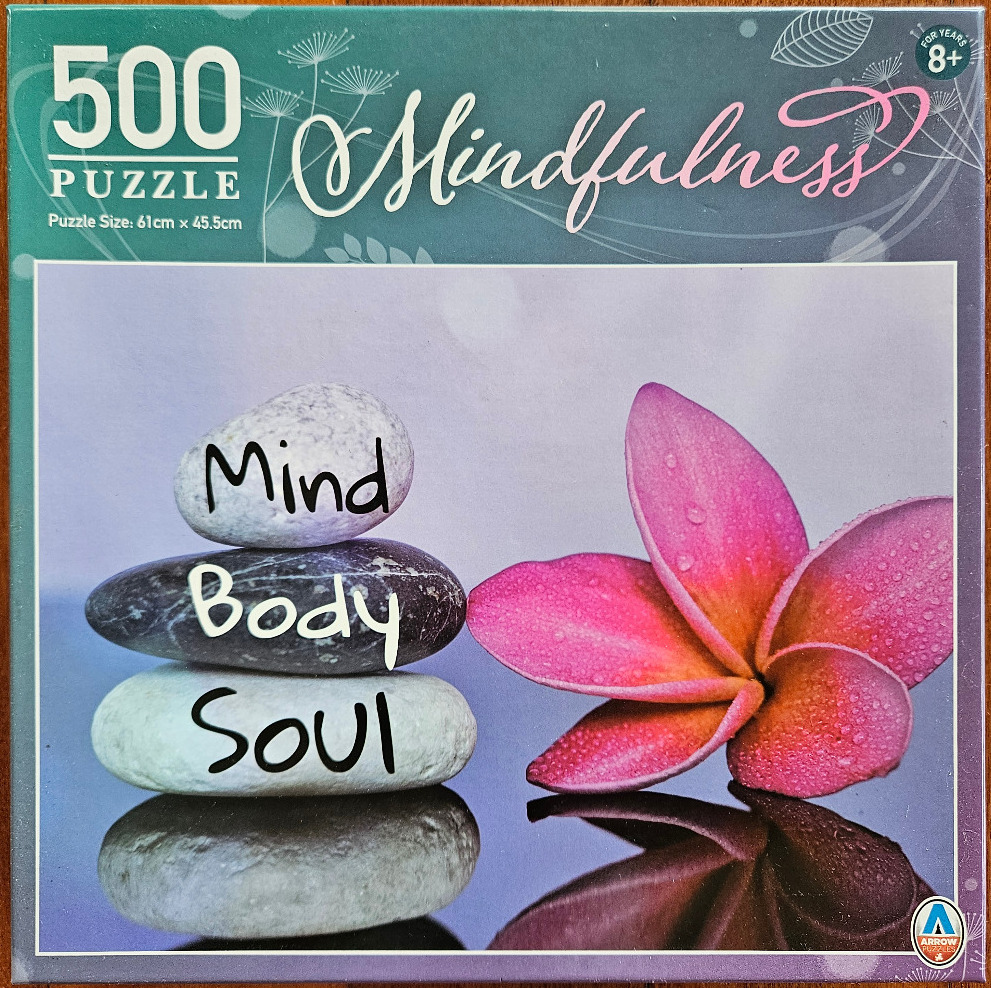 A stack of three balanced stones next to a pink plumeria flower against a soft purple background.