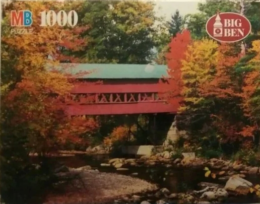 A red covered bridge surrounded by autumn trees over a rocky stream.