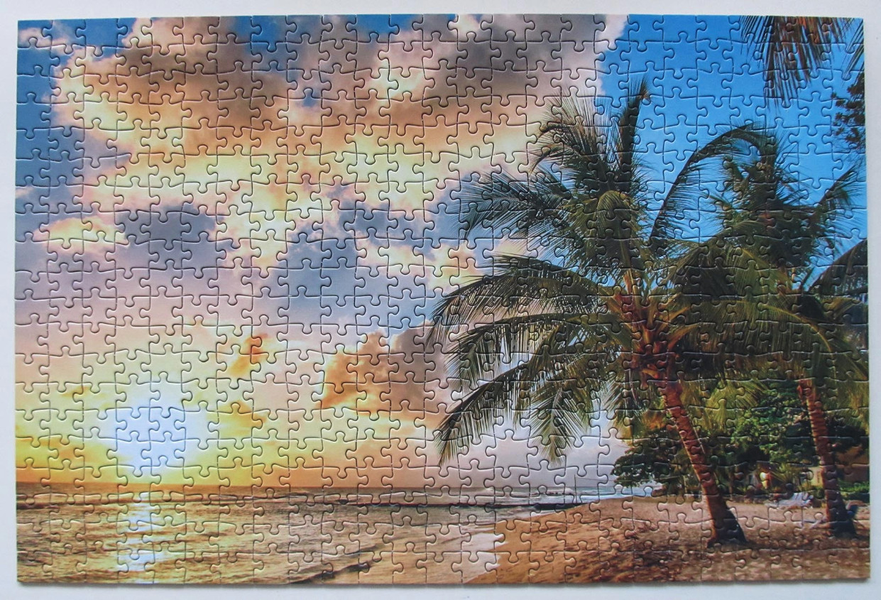 A tropical beach scene at sunset with palm trees silhouetted against a colorful, cloudy sky.