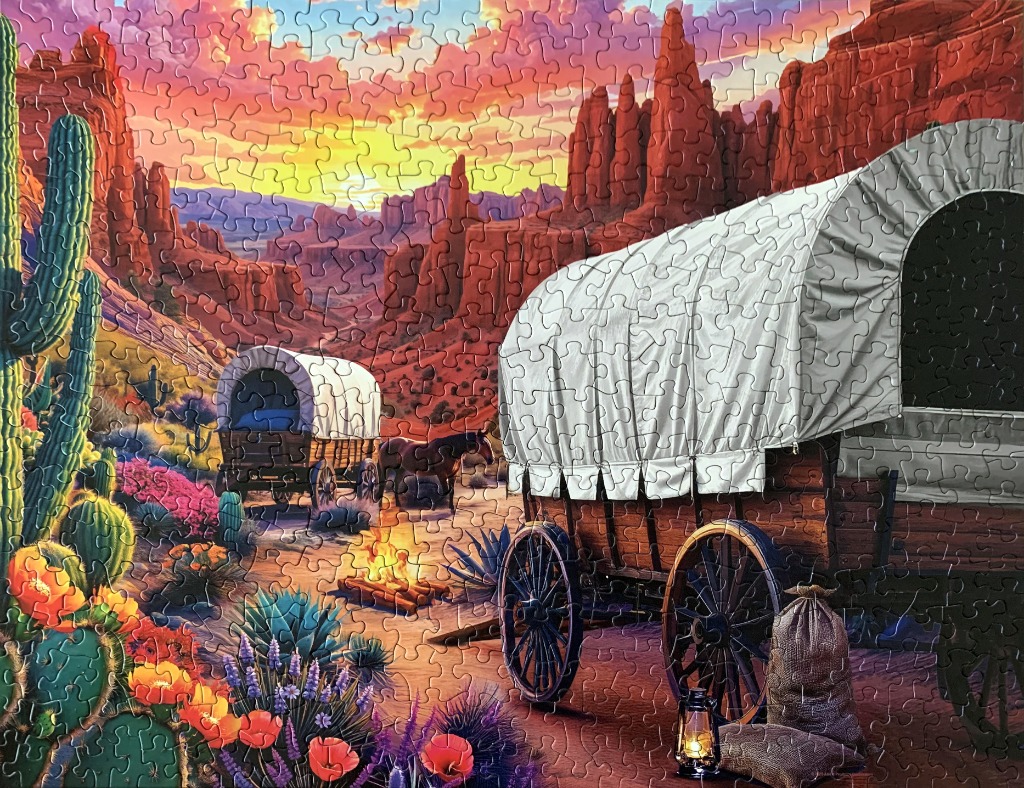A desert sunset scene with two covered wagons and cacti in the American West.