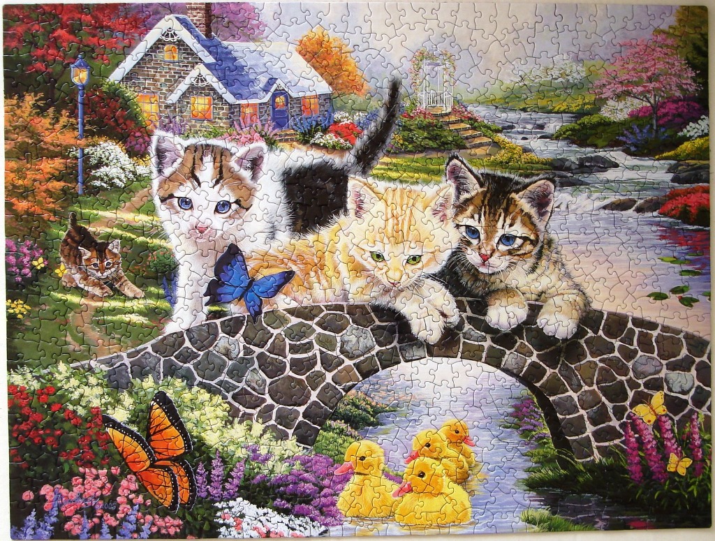 Three kittens playing on a stone bridge in a lush garden with a cottage and ducks