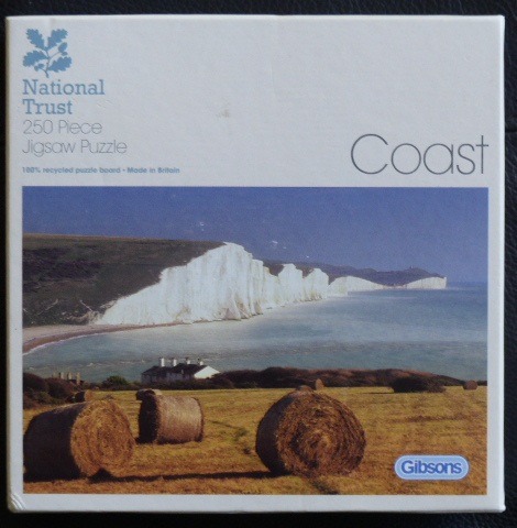 A scenic coastal landscape featuring white cliffs above a calm sea, with hay bales in a foreground field.