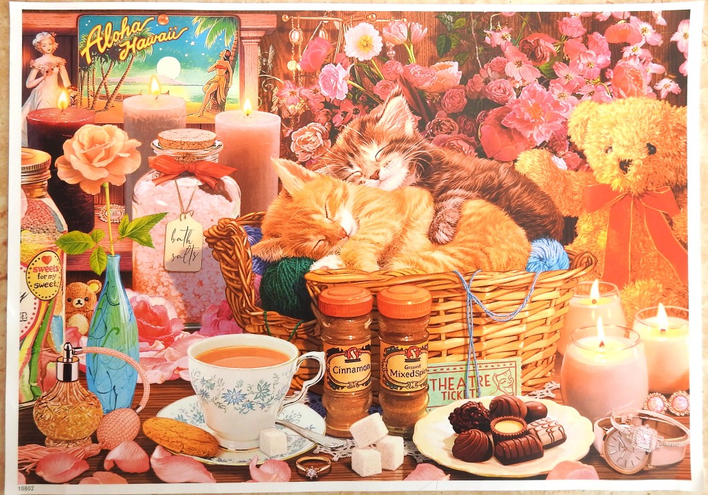 Two kittens sleeping in a wicker basket surrounded by candles, flowers, and sweets.