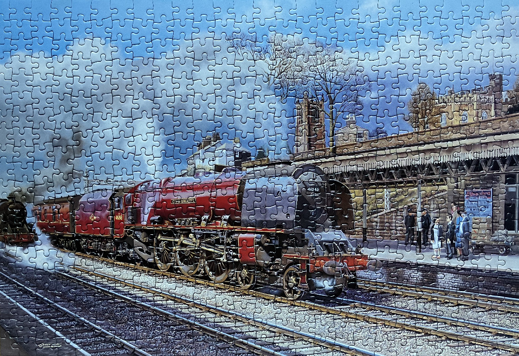 A red steam locomotive engine pulling into a station platform beneath a church tower.