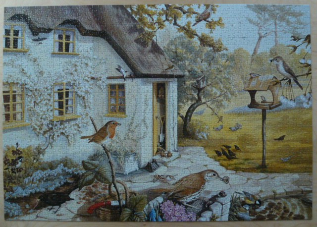 An illustration of a country cottage with a thatched roof, surrounded by many garden birds in a grassy yard.