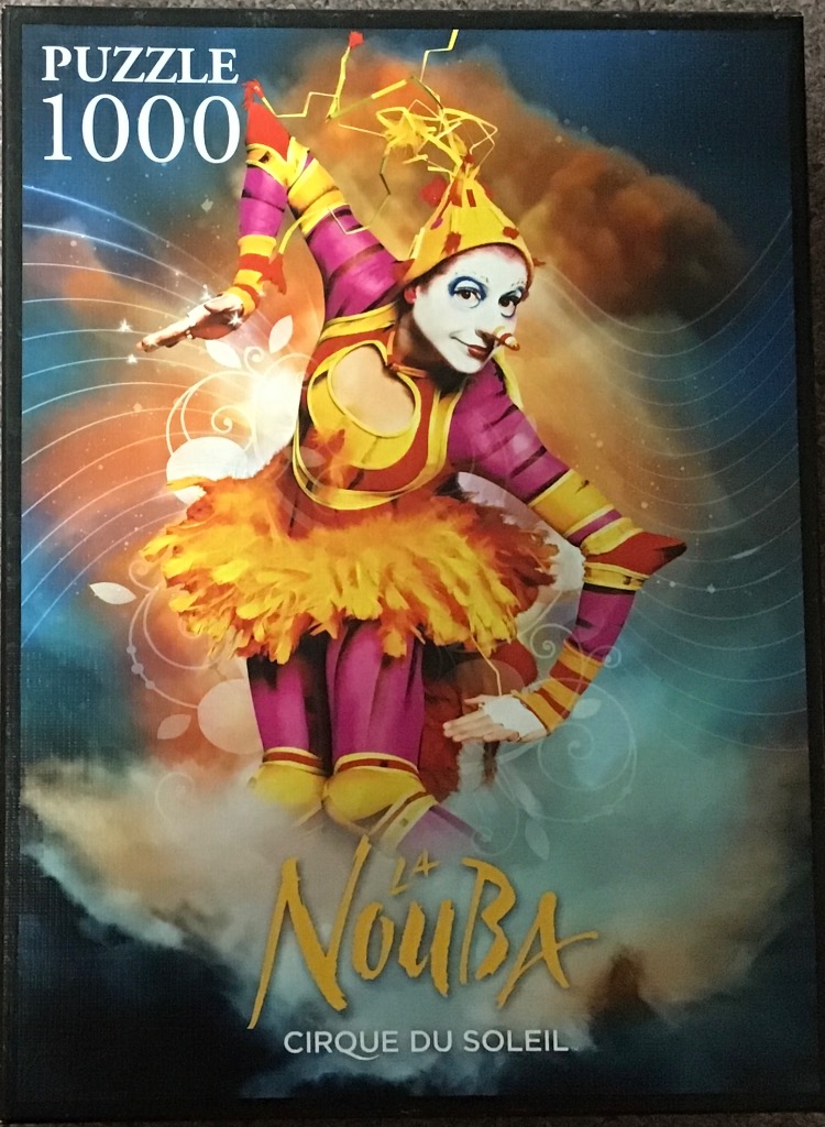A theatrical performer in a colorful costume and pointed hat posing against a dark, cloudy, and swirling background.
