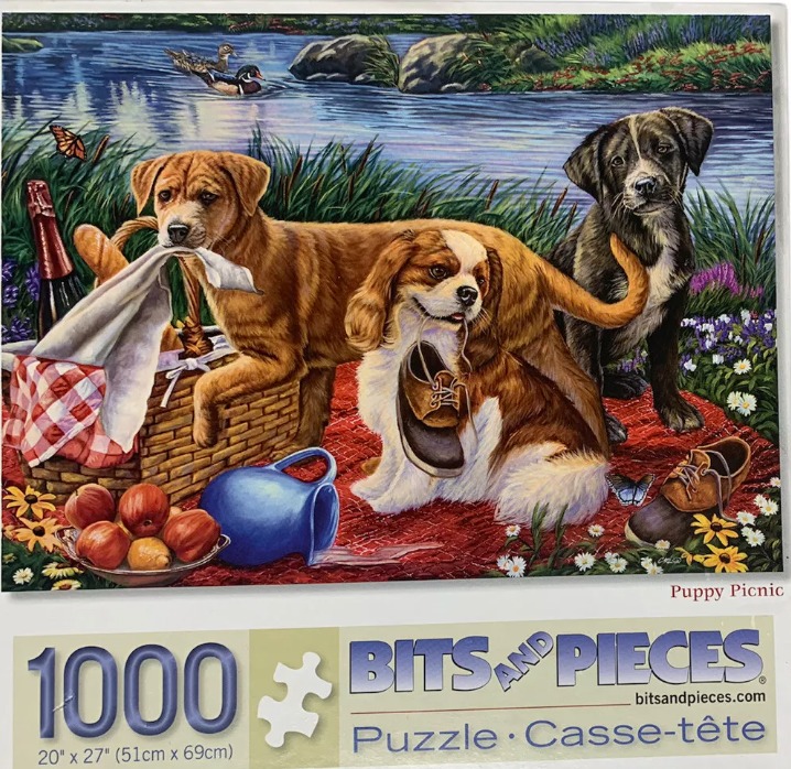 Three puppies enjoying a picnic by a lake with a wicker basket, food, and shoes.
