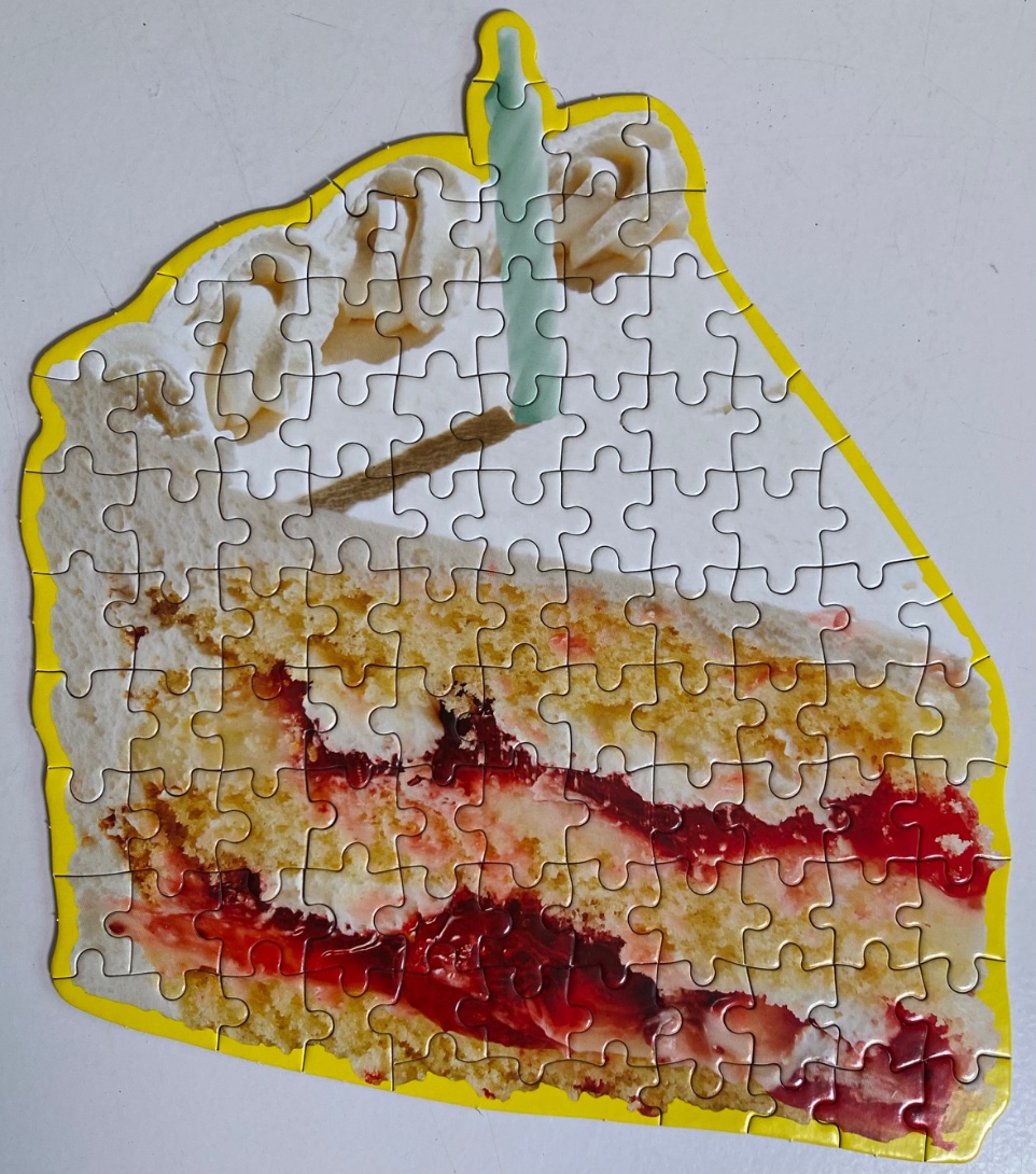 A slice of yellow cake with red jam filling, white frosting, and a single lit candle on top.