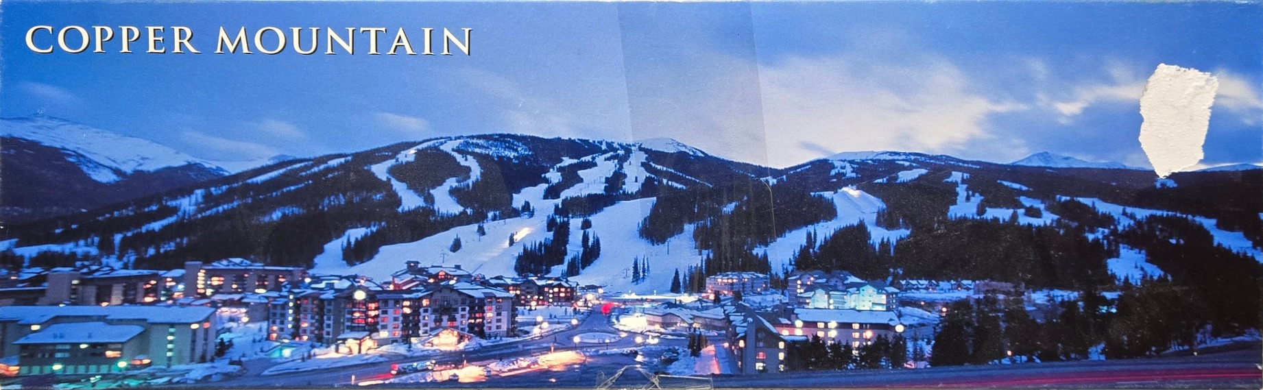 Panoramic view of Copper Mountain resort at dusk with snow-covered ski slopes and illuminated buildings.