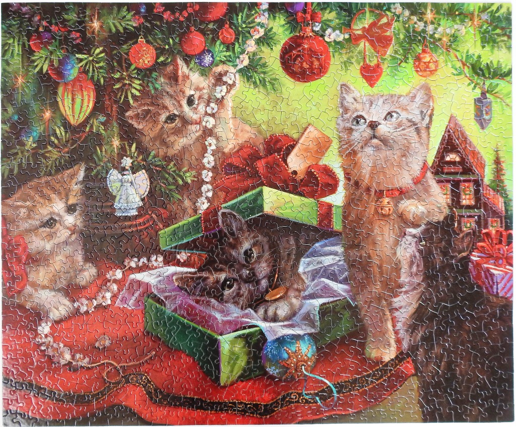 Four kittens play under a festive Christmas tree surrounded by wrapped gifts and ornaments.