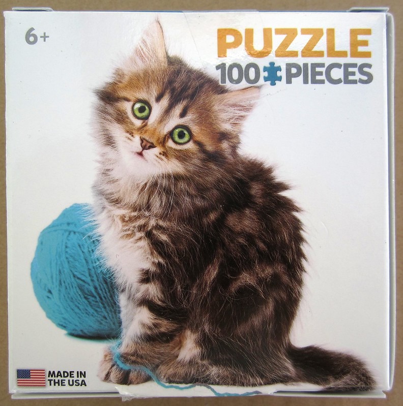 A fluffy brown tabby kitten with bright green eyes sitting next to a large ball of bright blue yarn.