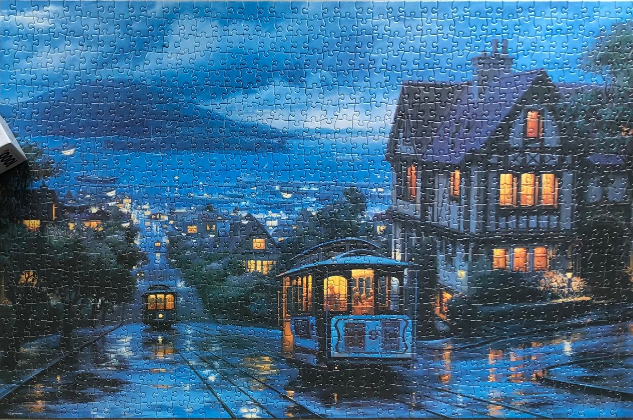 A classic cable car moves down a rainy city street at twilight past a half-timbered house.