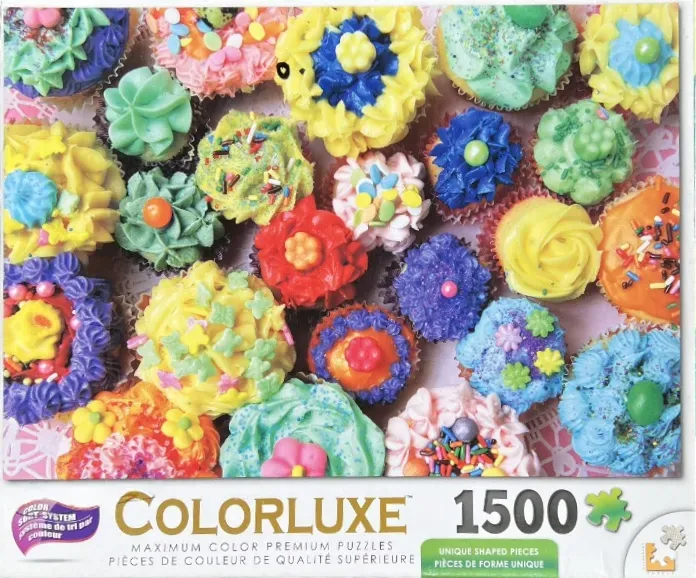 An overhead arrangement of many colorful frosted cupcakes decorated with sprinkles and sugar flowers.