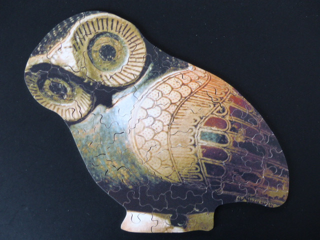 An owl shape featuring ancient Greek pottery style artwork of an owl on a black background.