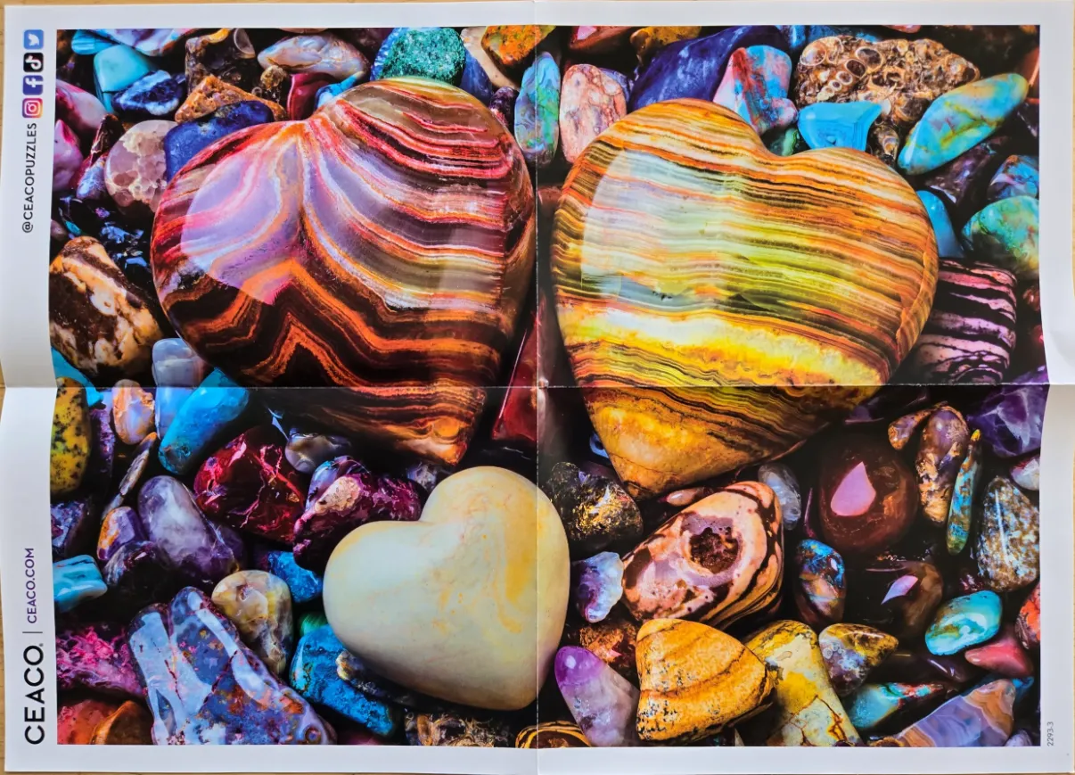 Three heart-shaped polished stones resting on a bed of colorful, assorted tumbled gems.