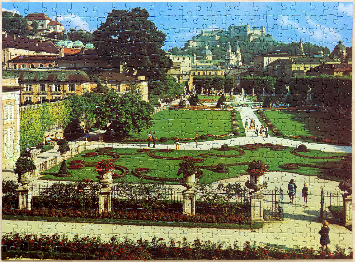 A sunny view of the Mirabell Gardens in Salzburg, Austria, with a fortress on the hill in the distance.