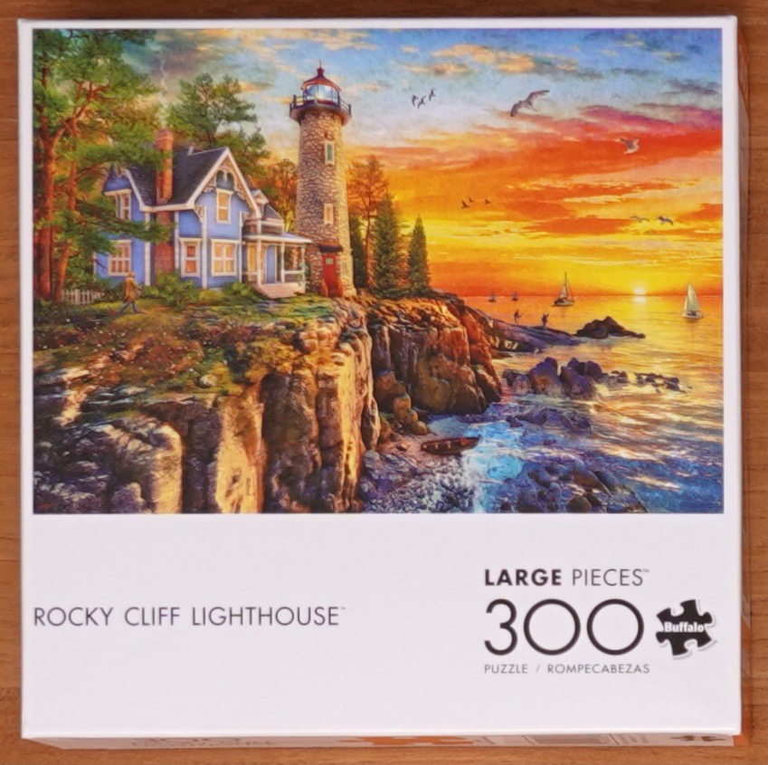 A lighthouse and blue Victorian house on a rocky cliff overlooking a sunset ocean scene.