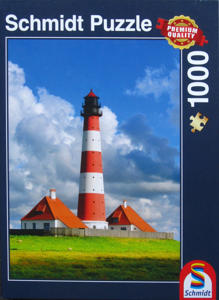 Tall red and white lighthouse and keeper houses on a grassy hill under a blue cloudy sky.