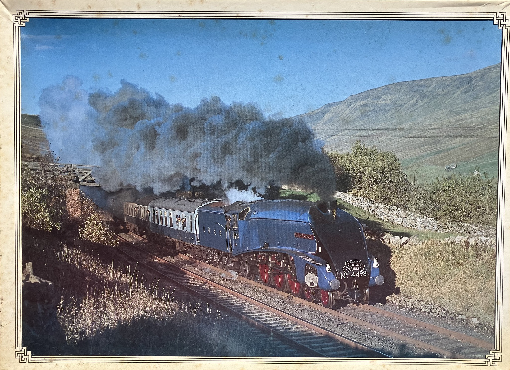 A vintage steam locomotive pulling passenger cars through a rural mountain landscape, emitting thick black smoke.