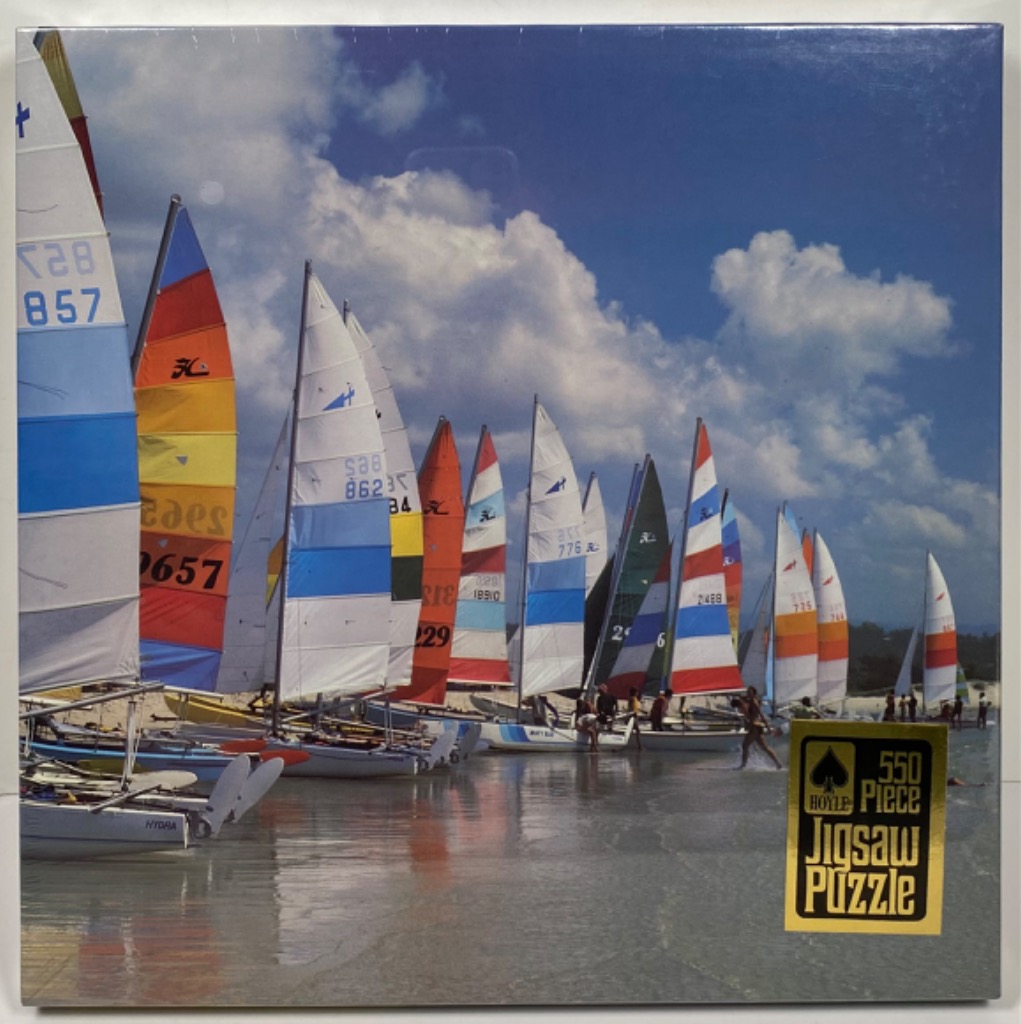 A row of colorful sailboats anchored in shallow water against a bright blue sky with fluffy white clouds.