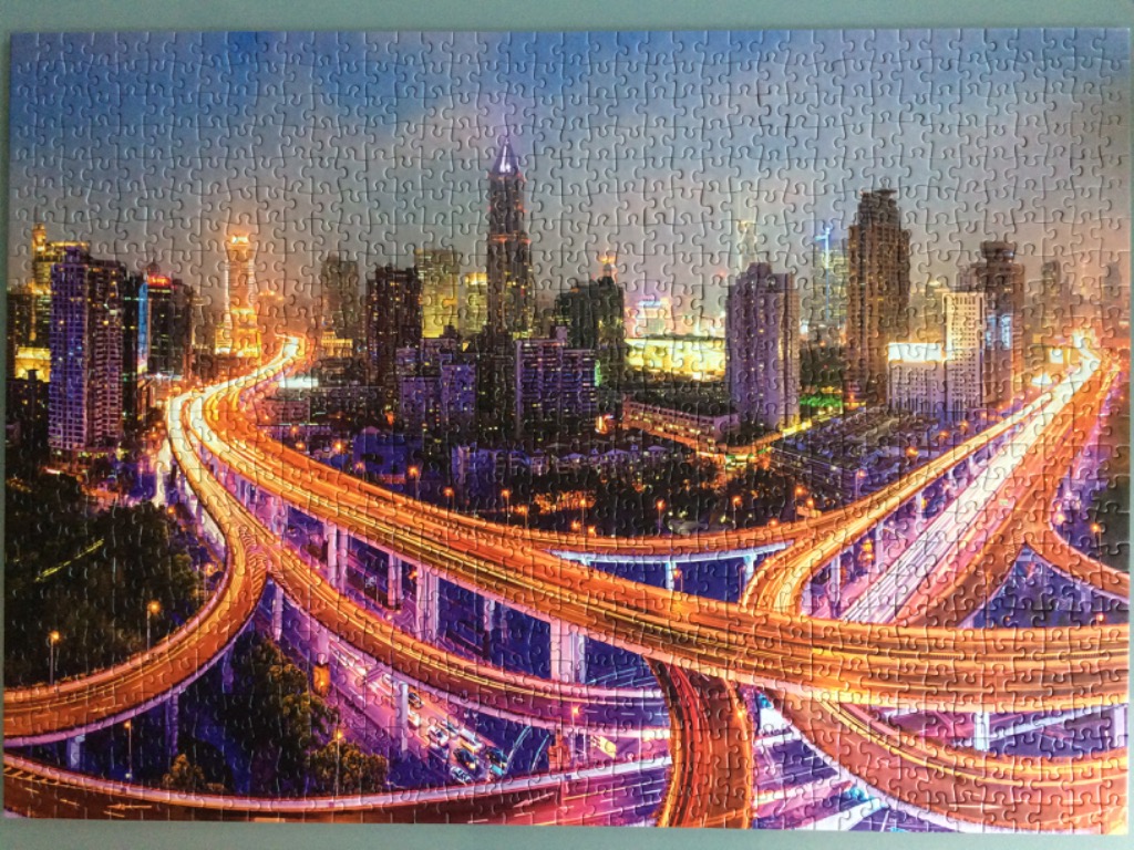 A panoramic aerial view of a brightly lit city skyline at night featuring multi-level highway overpasses.