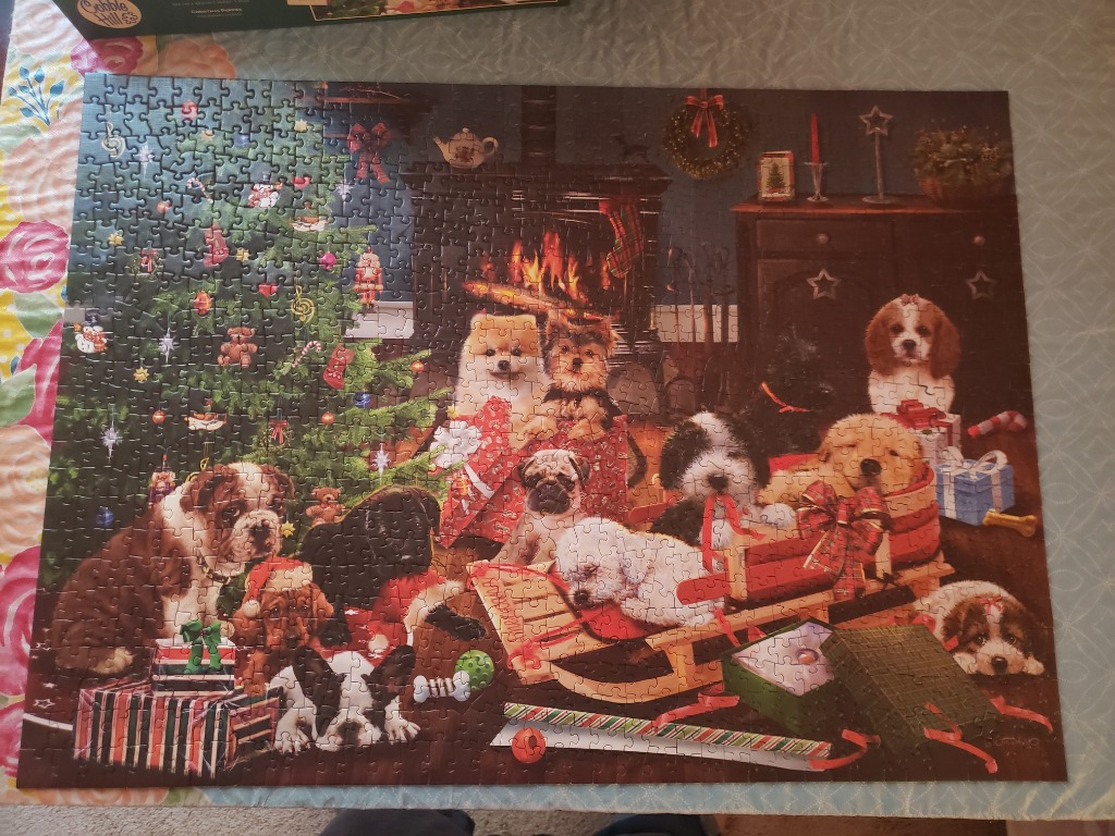 A warm, indoor scene featuring many different breeds of puppies gathered around a decorated Christmas tree and fireplace.
