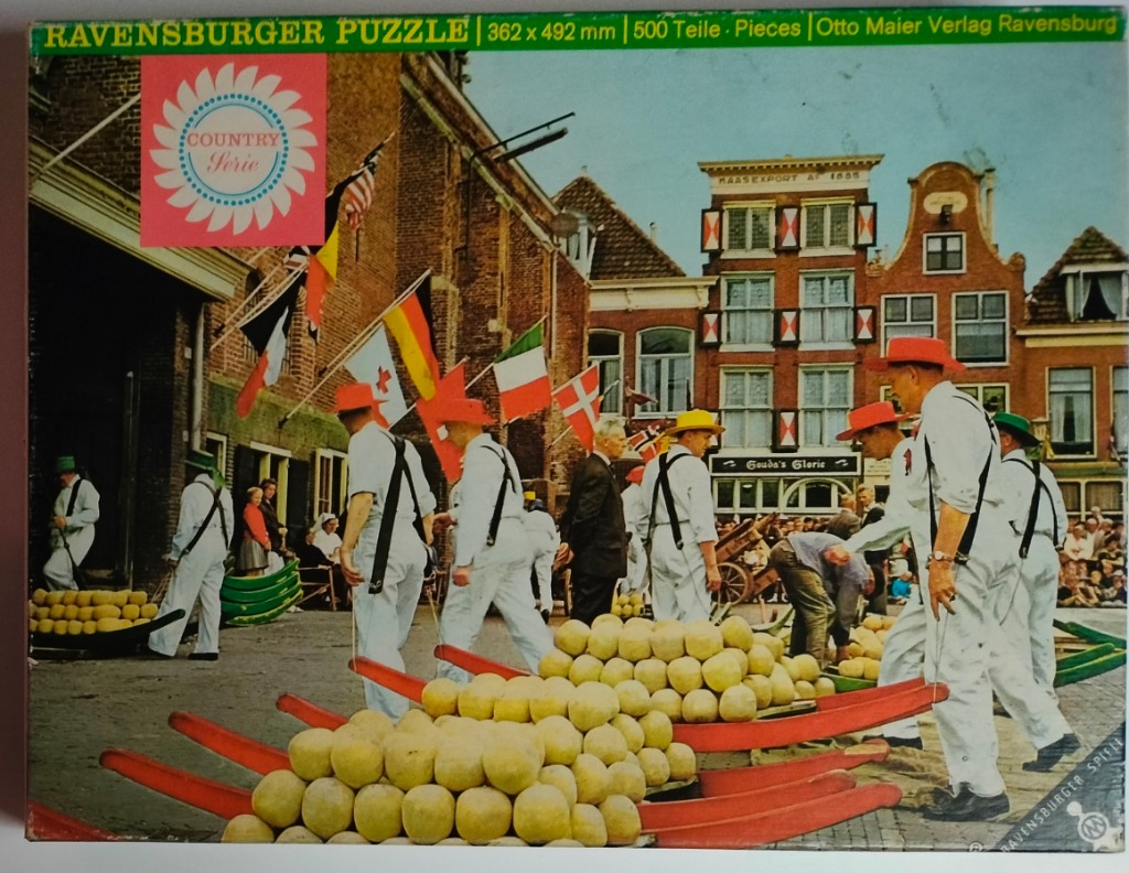 Men in white clothing carrying large wooden barrows filled with round yellow cheeses in a Dutch town square.