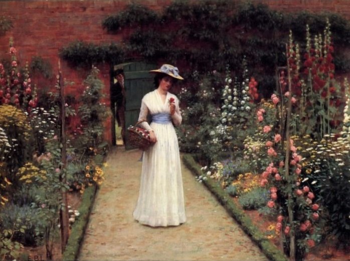 A woman in a white dress walking through a lush flower garden with a brick wall background.
