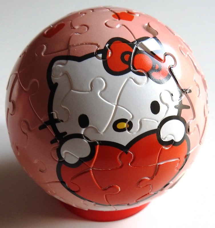 A spherical object featuring Hello Kitty holding a large red heart against a soft pink background.