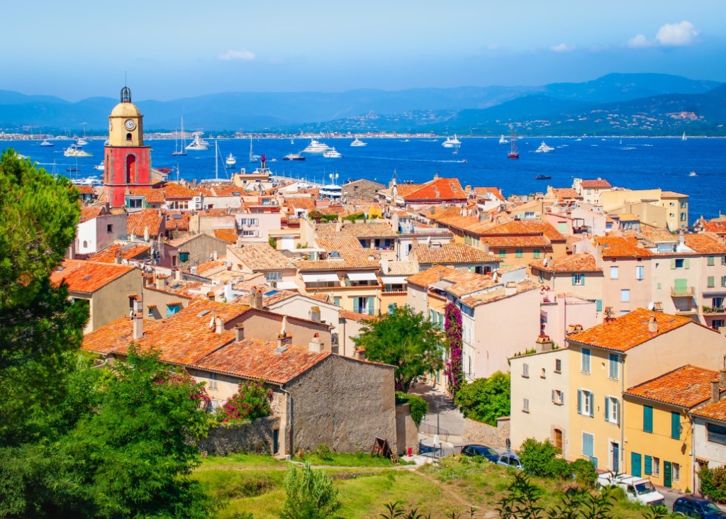 Sunlit coastal town of Saint-Tropez with red-tiled roofs overlooking a blue harbor filled with boats.