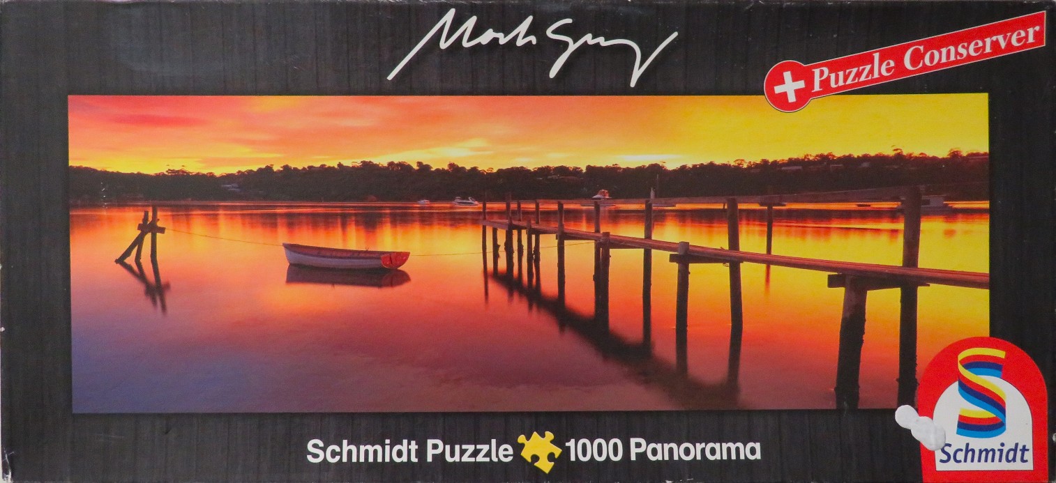 A panoramic landscape photo of a calm lake at sunset with a wooden pier and a small rowing boat.