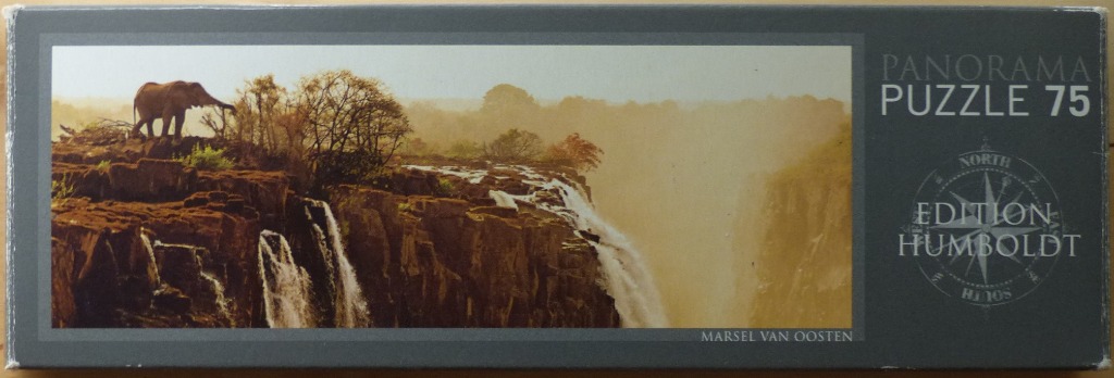 A lone elephant standing on a rocky cliff overlooking a massive, misty waterfall at sunset.