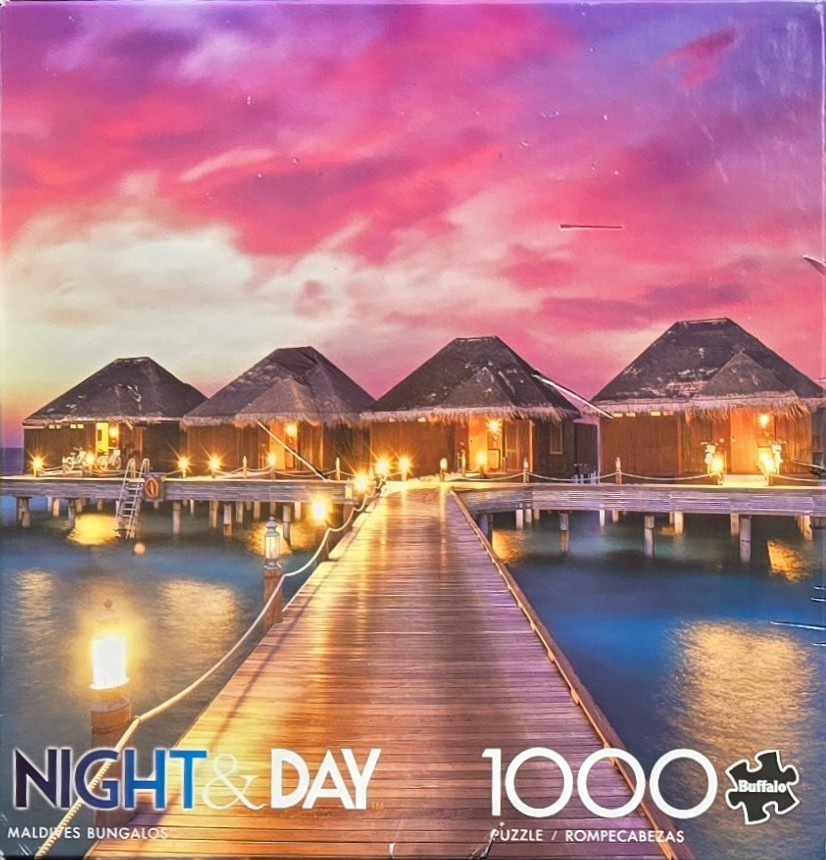 Overwater bungalows at sunset with a long wooden boardwalk leading to them over calm blue water.