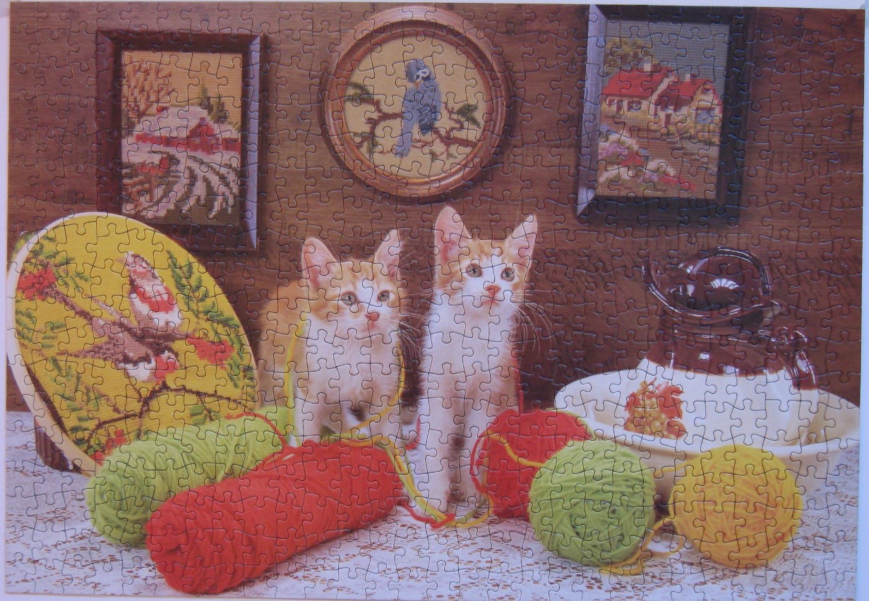Two ginger and white kittens sitting on a table with yarn and embroidered art.