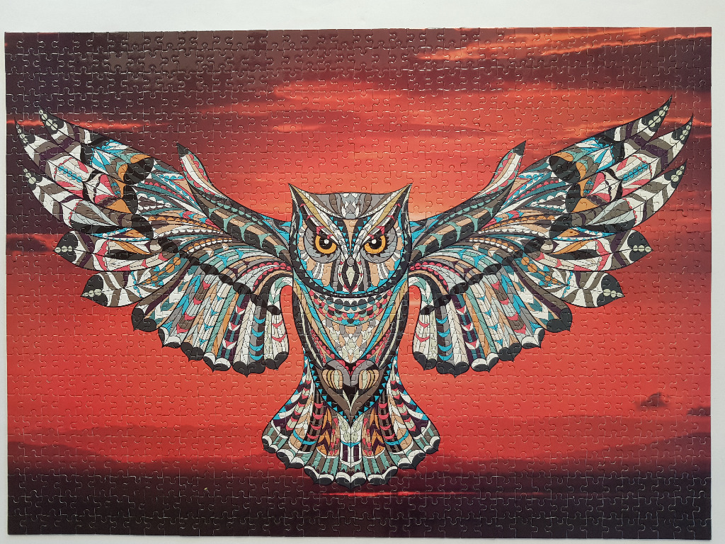 An owl with intricate tribal-style patterns on its wings flying against a deep red sunset sky.