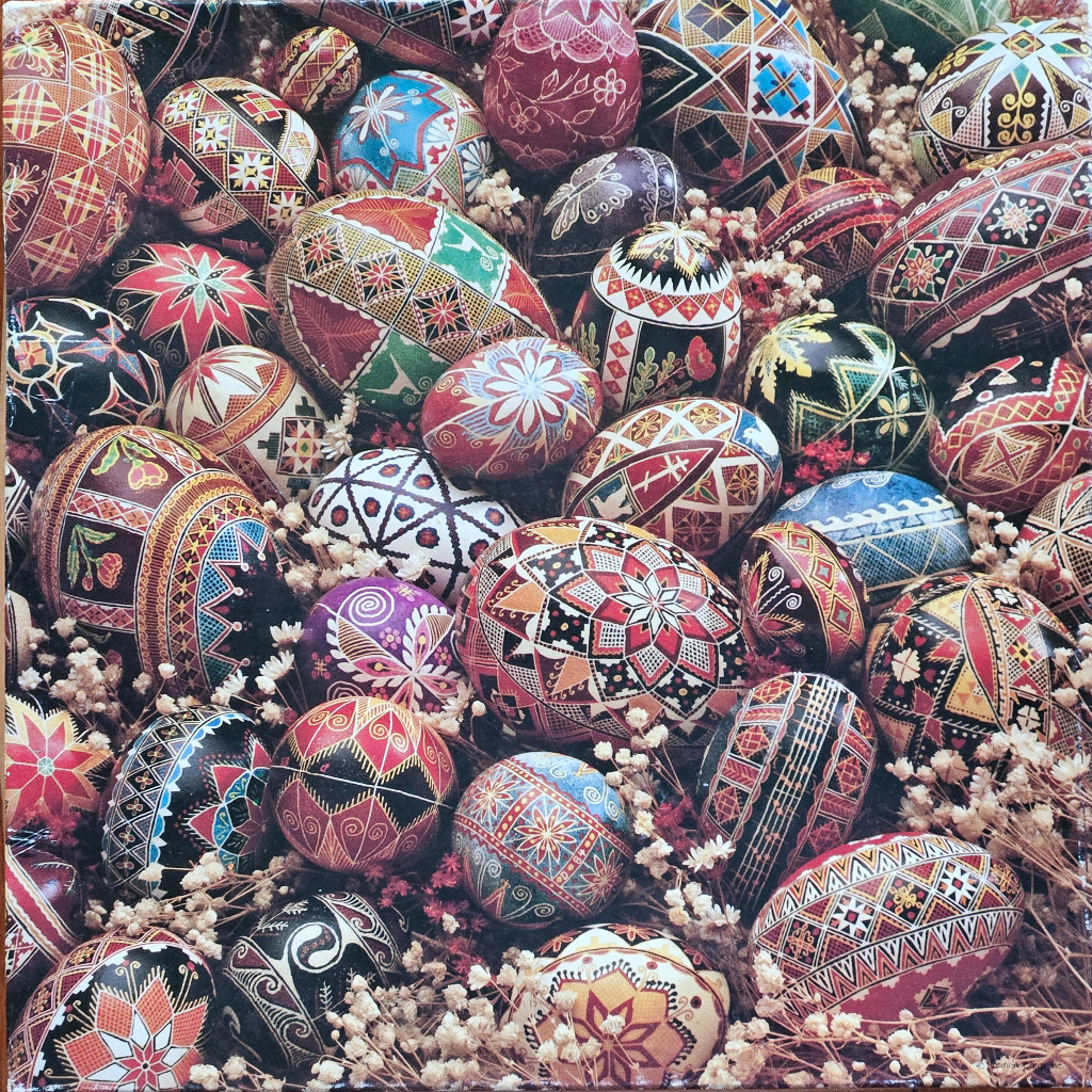 A close-up collection of intricately decorated, traditional Pysanka Easter eggs nestled among dried white baby