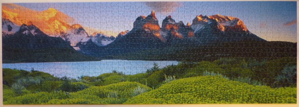 Panoramic mountain landscape at sunrise with a foreground of green bushes and a central blue lake.