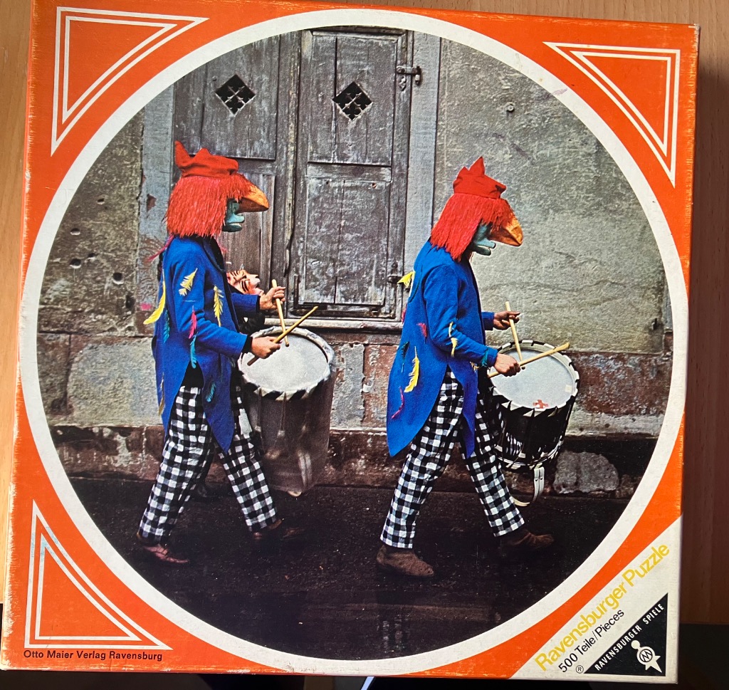 Two performers in traditional Swiss carnival costumes playing drums in front of an old wooden door.