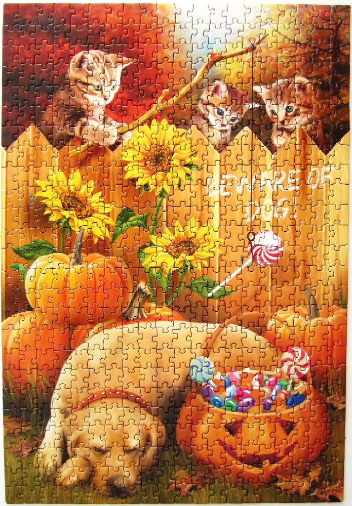 Three kittens peeking over a fence behind a resting golden retriever, sunflowers, pumpkins, and candy for Halloween.