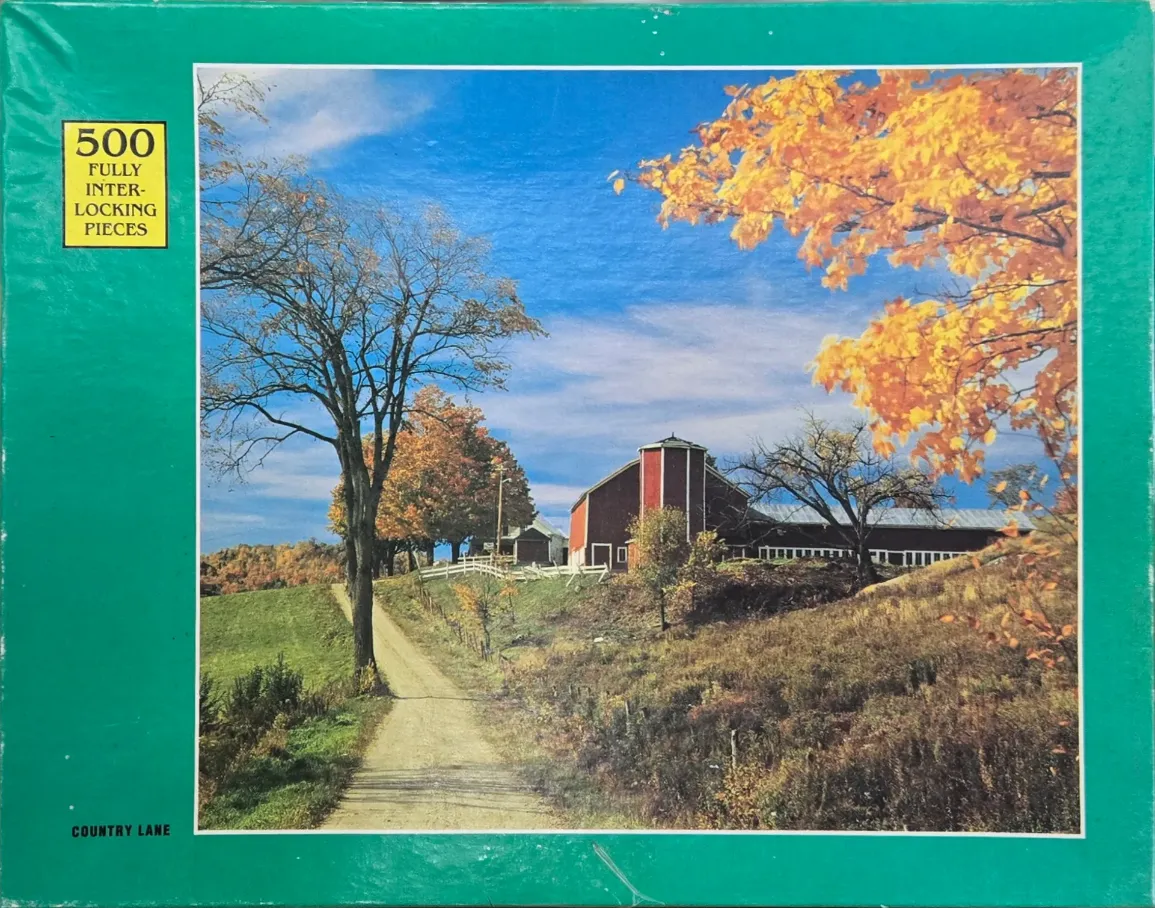 A dirt path leads toward a red barn on a hillside under a bright blue autumn sky.
