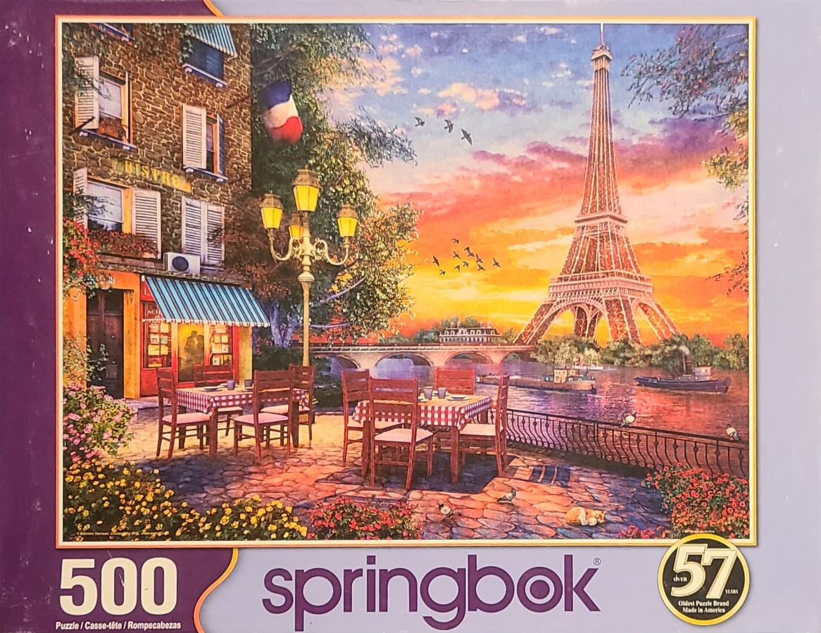 An outdoor bistro terrace overlooking the Eiffel Tower in Paris at sunset.