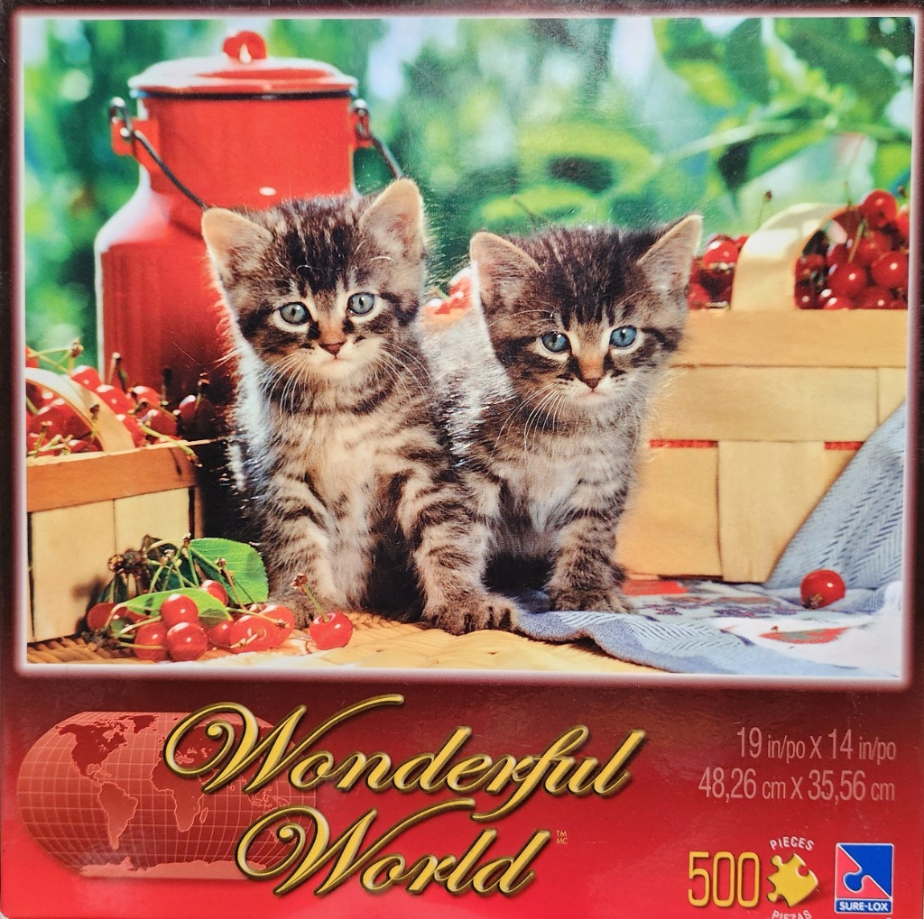 Two tabby kittens sitting between a red milk can and a basket of cherries